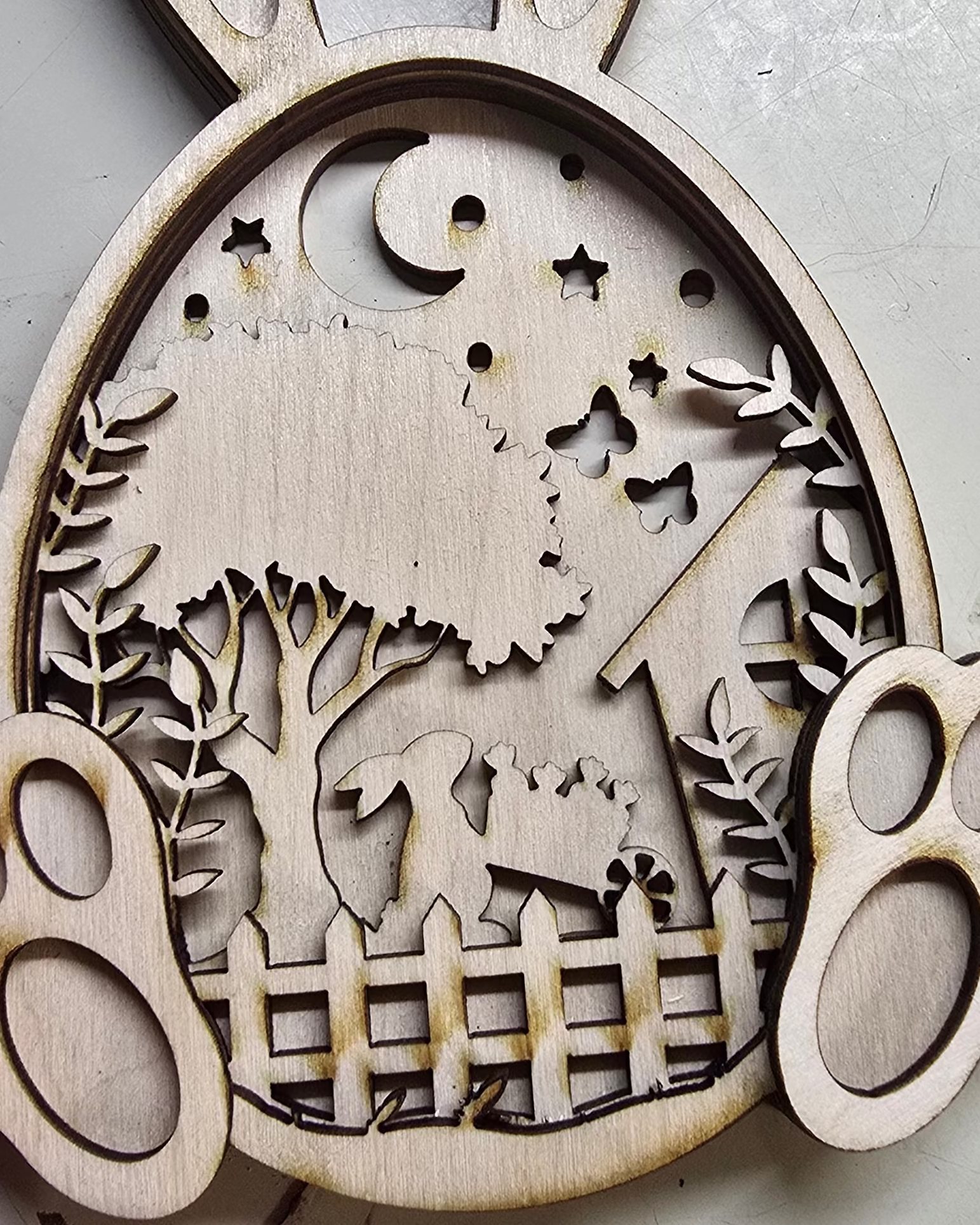 Wooden cutout with rabbit ears, a landscape design, and paw prints on a light background.